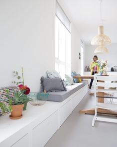 a woman standing in the kitchen next to a table with flowers and plants on it