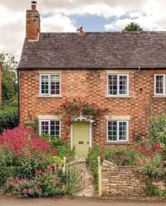 an old brick house with flowers growing on the front and side walls, surrounded by greenery