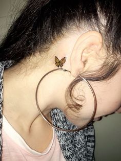 a woman wearing a pair of hoop earrings with a butterfly on the back of her ear