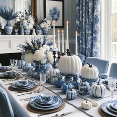 a dining room table set with blue and white dishes, pumpkins, candles and flowers