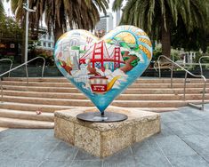 a heart shaped sculpture in the middle of steps with palm trees and buildings behind it