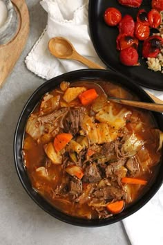 two black bowls filled with beef stew and carrots next to other food on a table