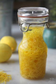 a glass jar filled with yellow noodles on top of a white counter next to lemons