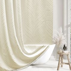 a white bathtub sitting next to a window covered in a curtain with feathers on it