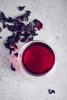 a glass cup filled with red liquid next to dried flowers on a white counter top