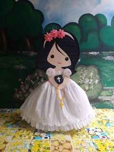 a paper doll in a white dress with a cross on it's chest and pink flower in her hair