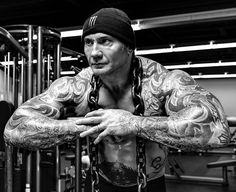 a man with tattoos is standing in front of a barbell exercise machine and looking at the camera