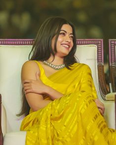 a woman in a yellow sari sitting on a white chair with her arms crossed