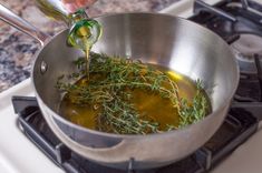 a person pouring olive oil into a pan on top of a stove with herbs in it