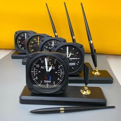 four clocks are sitting next to each other on a table with pen and pencils