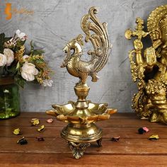 an ornate brass statue on top of a wooden table next to flowers and vases