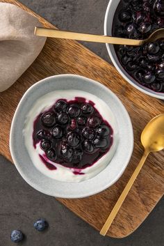 a bowl of yogurt with blueberries in it on a wooden cutting board