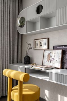 a yellow chair sitting in front of a desk with pictures on the wall behind it