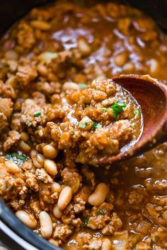 a wooden spoon scooping some food out of a slow cooker filled with beans