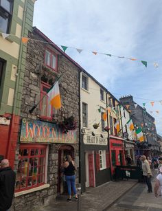 people are walking down the street in front of some buildings with flags hanging from them