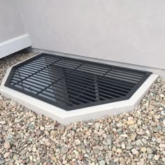 a drain grate sitting on top of gravel next to a wall with a door