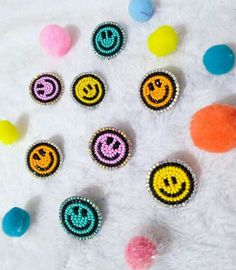 six embellishments with smiley faces and pom poms on a white surface