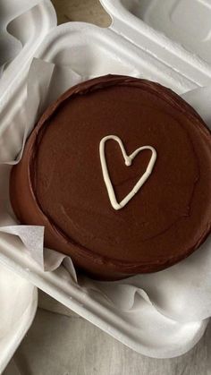 a chocolate cake with a heart on top in a white take - out container, ready to be eaten