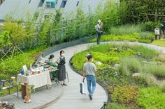 people are walking around an outdoor garden with various plants and food on the tables in front of them