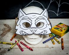 a white skull with a cat mask and crayons on the table next to it