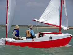 two people in a red and white sailboat on the water with one person wearing a hat