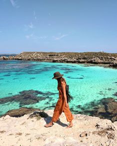 a woman standing on top of a rocky cliff next to the ocean with clear blue water