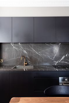 a kitchen with black cabinets and marble counter tops, along with a wooden dining table