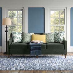 a living room with blue walls and green couch in the center, along with two windows