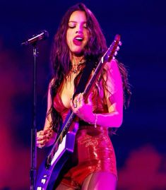 a woman with long dark hair holding a guitar and singing into a microphone on stage