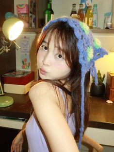 a young woman wearing a crocheted hat in front of a desk with a lamp