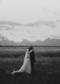 a bride and groom standing in the middle of a field with mountains in the background