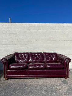 a red leather couch sitting in front of a white brick wall on the side of a building