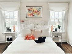 a laptop computer sitting on top of a white bed in a bedroom next to two windows