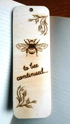 a wooden bookmark with an image of a bee and the words to be consumed on it