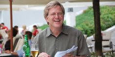 a man sitting at a table with a glass of wine and paper in his hand