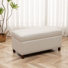 a white ottoman sitting on top of a wooden floor next to a potted plant