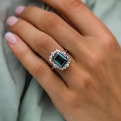 a woman's hand wearing a ring with an emerald and diamond center stone on it