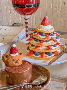 a stack of pancakes topped with strawberries and blueberries next to a glass of wine