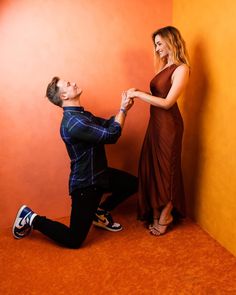 a man kneeling down next to a woman in a dress and high heels on the floor