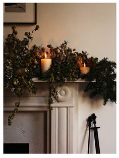 two candles are lit on top of a mantel decorated with greenery and ivy