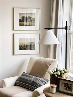 a living room with pictures on the wall and a chair next to a lamp in front of a window