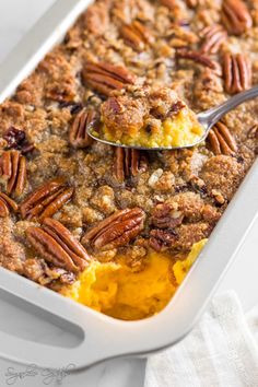 a casserole dish with pecans on top and a spoon in the casserole