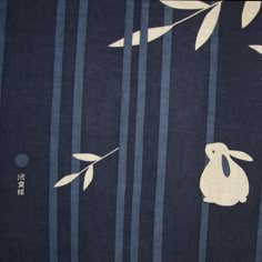 a blue and white striped fabric with a rabbit on it's back in front of bamboo branches