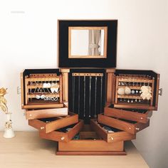 an open wooden jewelry box sitting on top of a table next to a vase and mirror