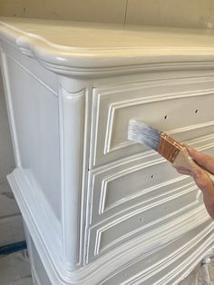 a person holding a paintbrush in their hand and painting the top of a dresser