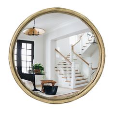 a living room with white walls and wooden stairs in the center is seen through a round mirror