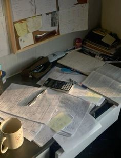 a cluttered desk with many papers and a calculator on it, next to a window