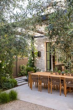 an outdoor dining area with wooden table and chairs, surrounded by greenery on either side