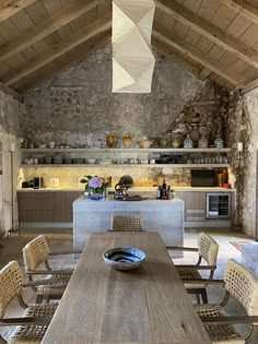 a table and chairs in a room with stone walls, exposed ceiling and open shelves