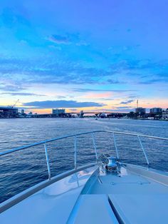 the back end of a boat traveling through the water at dusk with buildings in the background